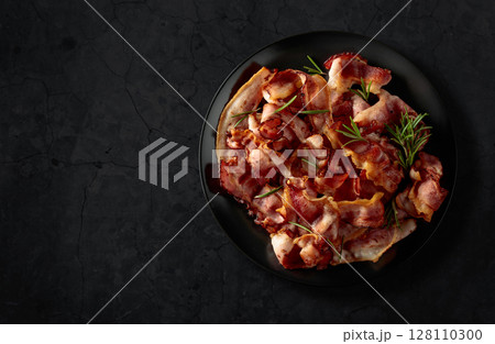 Fried bacon with rosemary on a black stone background. Fried bacon with rosemary on a black stone background. 128110300