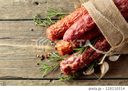 Various dry cured sausages with spices on a old wooden table. 128110314