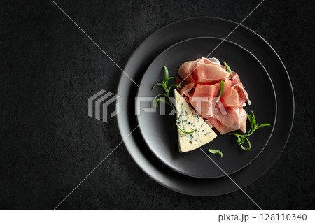 Blue cheese, prosciutto, and rosemary on a black table. Blue cheese, prosciutto, and rosemary on a black table. 128110340