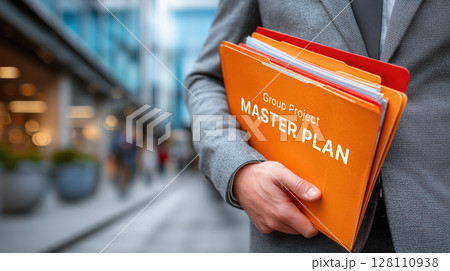 Person in suit holds orange folder labeled Group Project Master Plan in urban setting, symbolizing organization and teamwork 128110938