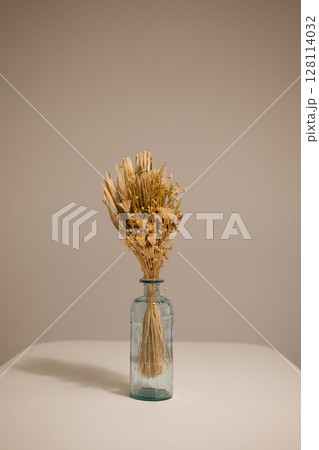 Close up of dried floral bouquet in blue glass vase centered on a white table against neutral wall 128114032