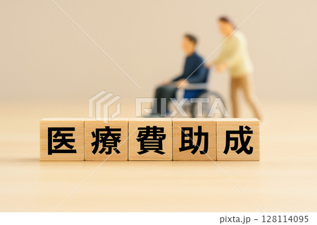 医療費助成の文字ブロックと車椅子の男性を表現したミニチュア構成 医療費助成の文字ブロックと車椅子の男性を表現したミニチュア構成 128114095