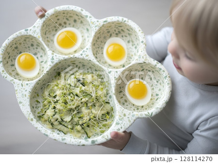 A young kid seated at the kids' table will be consuming nutritious food made from sprouted grains and eggs, along with vegetarian microgreens, all rich in vitamins and minerals, as seen from above 128114270