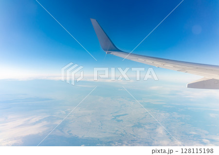 View from the airplane window at a beautiful blue clear sky, earth, sea and the airplane wing View from the airplane window at a beautiful blue clear sky, earth, sea and the airplane wing 128115198