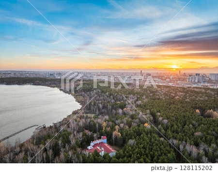 Autumn forest on lake shore at sunset and city on horizon, aerial view 128115202