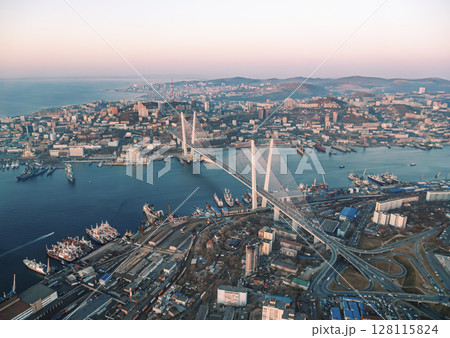 Aerial cityscape of Vladivostok at sunset showcasing urban development and the famous bridge connecting urban areas 128115824