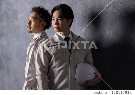 笑顔で黒壁の前に立つ作業服の男性 128115939