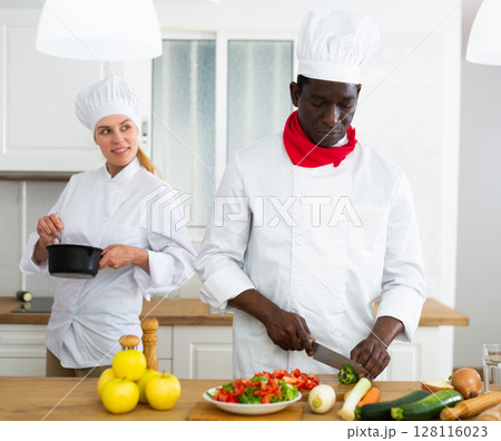 Professional chef in white uniform working with female assistant in private kitchen Professional chef in white uniform working with female assistant in private kitchen 128116023