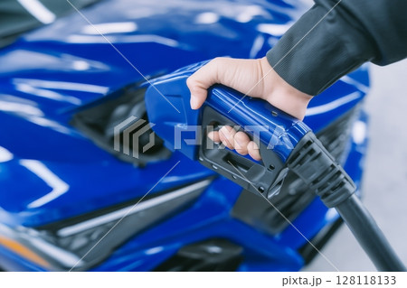 A charging station for electric vehicles, where a person is manually charging an electric car using a plugged-in power cable, with a flare light effect 128118133