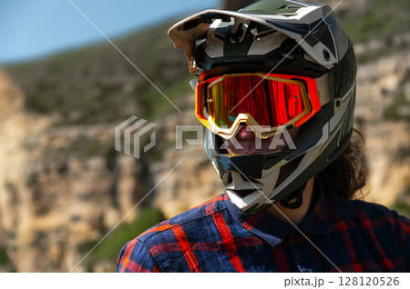Close-up portrait of young sportsman wearing protective helmet and protective mask on his face. Mature guy resting looking at camera after hard training in mountains Close-up portrait of young sportsman wearing protective helmet and protective mask on his face. Mature guy resting looking at camera after hard training in mountains 128120526