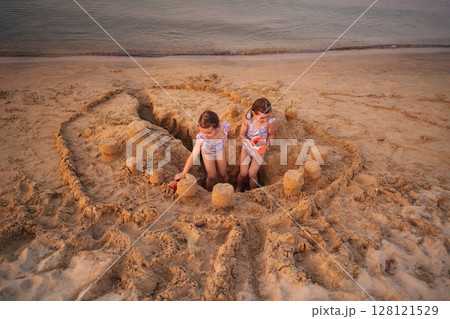Sisters building a grand sandcastle at sunset on the beach Sisters building a grand sandcastle at sunset on the beach 128121529