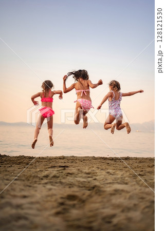 Joyful children leap into the air at a serene beach sunset 128121530