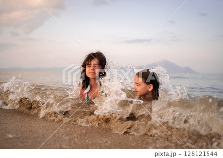 Sisters enjoying the waves during a sunny beach day at sunset 128121544