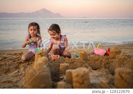 Joyful children building sandcastles at sunset on a tranquil beach Joyful children building sandcastles at sunset on a tranquil beach 128122670
