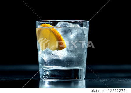 This striking cocktail features clear ice and a vibrant orange slice, elegantly displayed against a dark backdrop in a studio environment 128122754