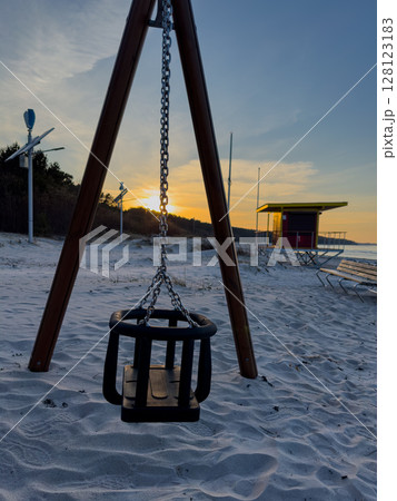 Swing set on sandy beach with sunset backdrop near lifeguard station and calm waters in the evening Swing set on sandy beach with sunset backdrop near lifeguard station and calm waters in the evening 128123183