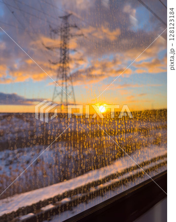 Sunset view from a train window with raindrops against the glass in a snowy landscape 128123184