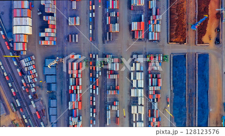 Bird's eye view of the port cargo area with containers, bulk cargo, cranes, trucks and forklifts. Evening industrial landscape at sunset. 128123576