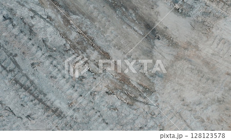 Aerial view of dry cracked ground with visible tire tracks, showing drought-affected soil and erosion patterns in a barren landscape 128123578