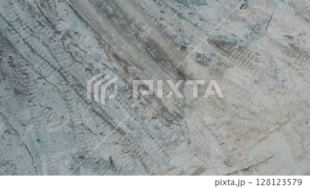 Top down view of dry cracked ground with visible tire tracks, showing drought-affected soil and erosion patterns in a barren landscape. Top down view of dry cracked ground with visible tire tracks, showing drought-affected soil and erosion patterns in a barren landscape. 128123579