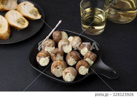Escargot bourguignon with butter and garlic. Traditional French dish made from snails, served with baguette and white wine. Selective focus, close-up, black background. Escargot bourguignon with butter and garlic. Traditional French dish made from snails, served with baguette and white wine. Selective focus, close-up, black background. 128123926