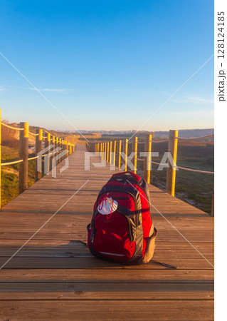 Backpack with pilgrim scallop shell (symbol of Camino de Santiago) on a wooden boardwalk. Pilgrimage concept. Way of St James, Camino de Santiago Backpack with pilgrim scallop shell (symbol of Camino de Santiago) on a wooden boardwalk. Pilgrimage concept. Way of St James, Camino de Santiago 128124185