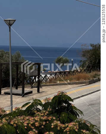 Sunny Greek coastal road lined with flowering plants and a distant sea view, perfect for travel, lifestyle, and scenic visuals. Sunny Greek coastal road lined with flowering plants and a distant sea view, perfect for travel, lifestyle, and scenic visuals. 128125538