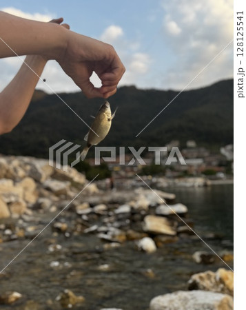 Hand Holding Tiny Fish at Rocky Shore Hand Holding Tiny Fish at Rocky Shore 128125541
