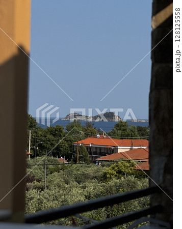 Framed view from a balcony showing rooftops, green hills, and the sea in the distance, perfect for vacation and landscape themes. Framed view from a balcony showing rooftops, green hills, and the sea in the distance, perfect for vacation and landscape themes. 128125558