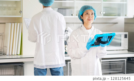 厨房をチェックする衛生白衣を着た男女作業員 128125645