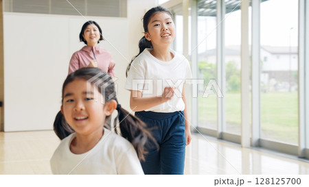体育館の中を走る女の子と女性教師 128125700