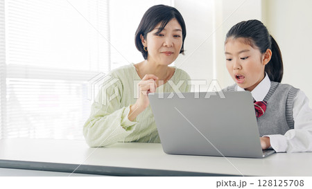 教室で女性教員からパソコンを教わる女の子 128125708