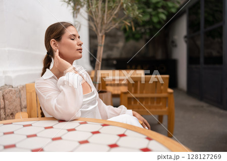 Woman Relaxation Garden: Pensive woman relaxes with closed eyes in outdoor cafe during sunny daytime. 128127269