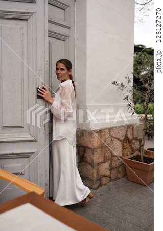 Fashion Model Door: Woman, wearing white, unlocks a grey door outside to enter building during daylight. Fashion Model Door: Woman, wearing white, unlocks a grey door outside to enter building during daylight. 128127270