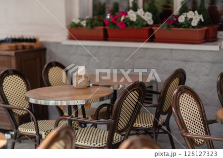 Tables Chairs Flowers: Outdoor cafe seating with wooden chairs, tables, and flowers for relaxed dining anytime. Tables Chairs Flowers: Outdoor cafe seating with wooden chairs, tables, and flowers for relaxed dining anytime. 128127323