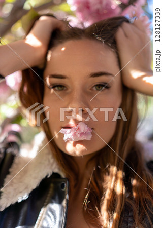 Sakura Woman Portrait: Girl holds blossom in mouth outside during springtime for artistic expression. Sakura Woman Portrait: Girl holds blossom in mouth outside during springtime for artistic expression. 128127339
