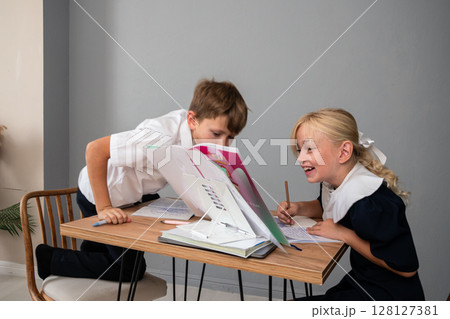 Children School Homework Classroom - Two children in school uniforms doing homework together at a desk in a classroom. Children School Homework Classroom - Two children in school uniforms doing homework together at a desk in a classroom. 128127381