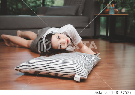 Top view of young beautiful asian woman with headphone and listening music from smartphone while lying on the floor at home. Top view of young beautiful asian woman with headphone and listening music from smartphone while lying on the floor at home. 128127575