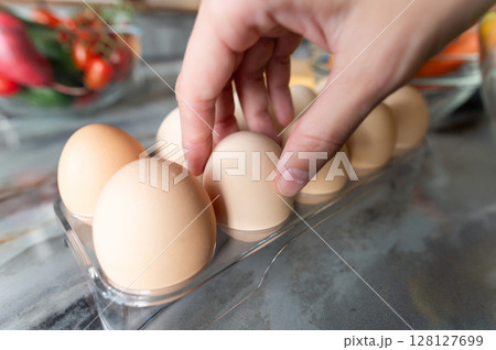 Human hand with eggs takes or puts one clean egg on the background of kitchen table with prepared ingredients. Food preparation concept Human hand with eggs takes or puts one clean egg on the background of kitchen table with prepared ingredients. Food preparation concept 128127699
