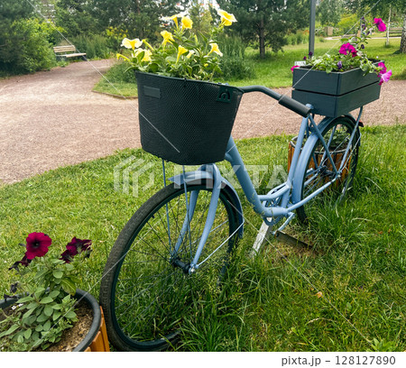 Vintage bicycle with flower planters in baskets, parked on grass, surrounded by greenery, showcasing a blend of nature and urban charm in a serene outdoor setting 128127890