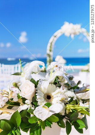 Bunch of flowers in a vase for wedding ceremony and beautiful wedding arch on a tropical beach 128127975