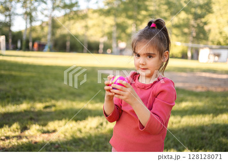 Cute little girl is holding a ball on the playground 128128071