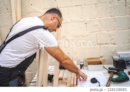 Mature male carpenter using electric screwdriver on a wooden plank outdoors Mature male carpenter using electric screwdriver on a wooden plank outdoors 128128083
