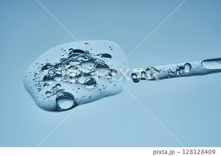 The texture of serum with spicules in a dropper on a blue background. The texture of serum with spicules in a dropper on a blue background. 128128409