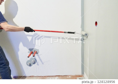 A close-up of a man's hand painting a wall white with a paint roller. Apartment painting, renovation. With space to copy. High quality photo 128128956