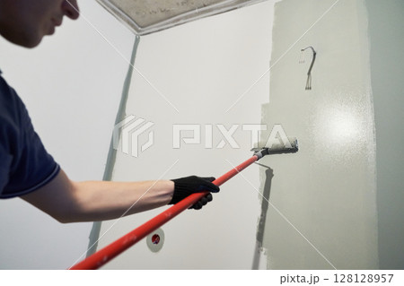 A worker paints the inner wall of his house. Apartment renovation. Concrete walls are painted gray with a paint roller. High quality photo A worker paints the inner wall of his house. Apartment renovation. Concrete walls are painted gray with a paint roller. High quality photo 128128957
