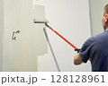 Men's hands paint walls with a roller, work painting on the surface, painting walls in an apartment, repair with white paint. With space to copy. High quality photo 128128961