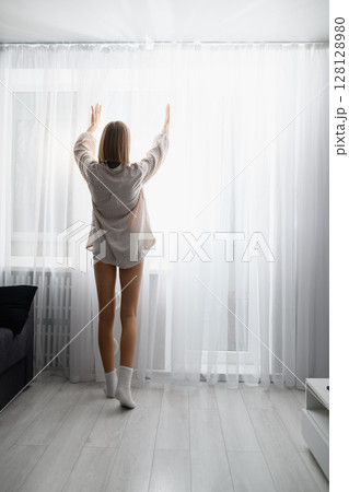 Young woman opening curtains to bright morning light at home. Young woman opening curtains to bright morning light at home. 128128980