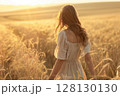Graceful woman enjoying a golden wheat field in the sunshine, gently brushing her hands through the grains as the breeze lifts her white dress. 128130130