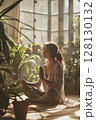 A calm woman meditates in the warmth of morning light, surrounded by green foliage and natural textures in a serene home space. 128130132
